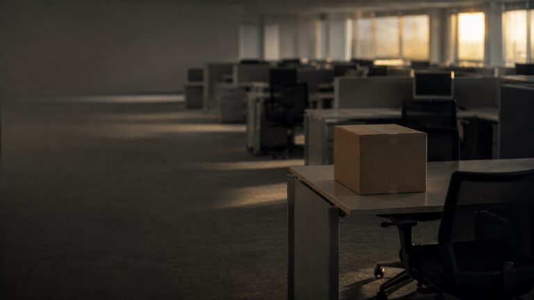 A lone cardboard box on an empty office desk after a round of layoffs